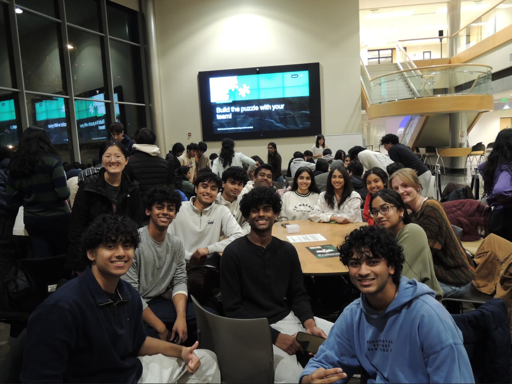 A Hack the Future team smiling together under a screen that reads Build the puzzle with your team