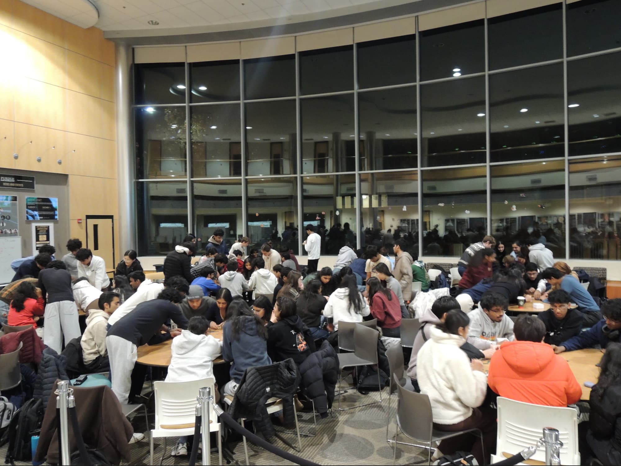Hack the Future members working together at tables across a glass-walled atrium during a club event